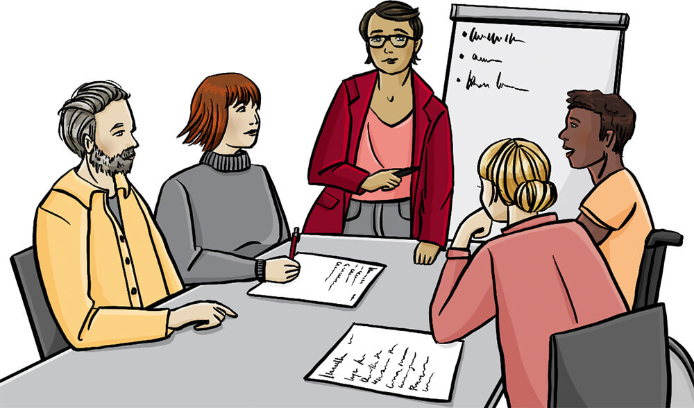 Menschen sitzen an einem Tisch und eine Frau erklärt ihnen etwas.